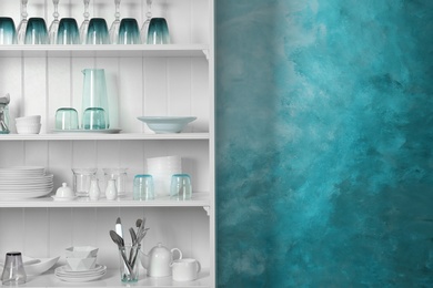 Photo of White shelving unit with set of dishware near color wall. Space for text