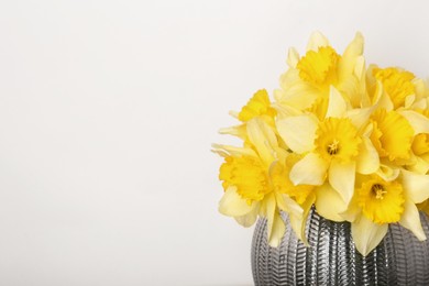 Bouquet of beautiful yellow daffodils in vase near beige wall. Space for text