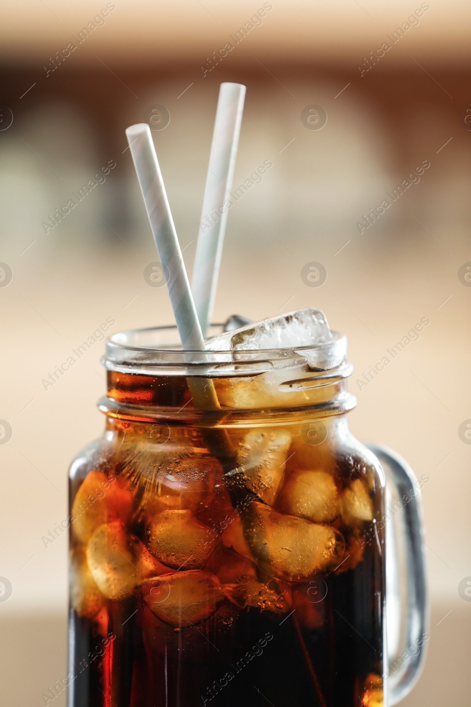 Photo of Mason jar of cola with ice against blurred background