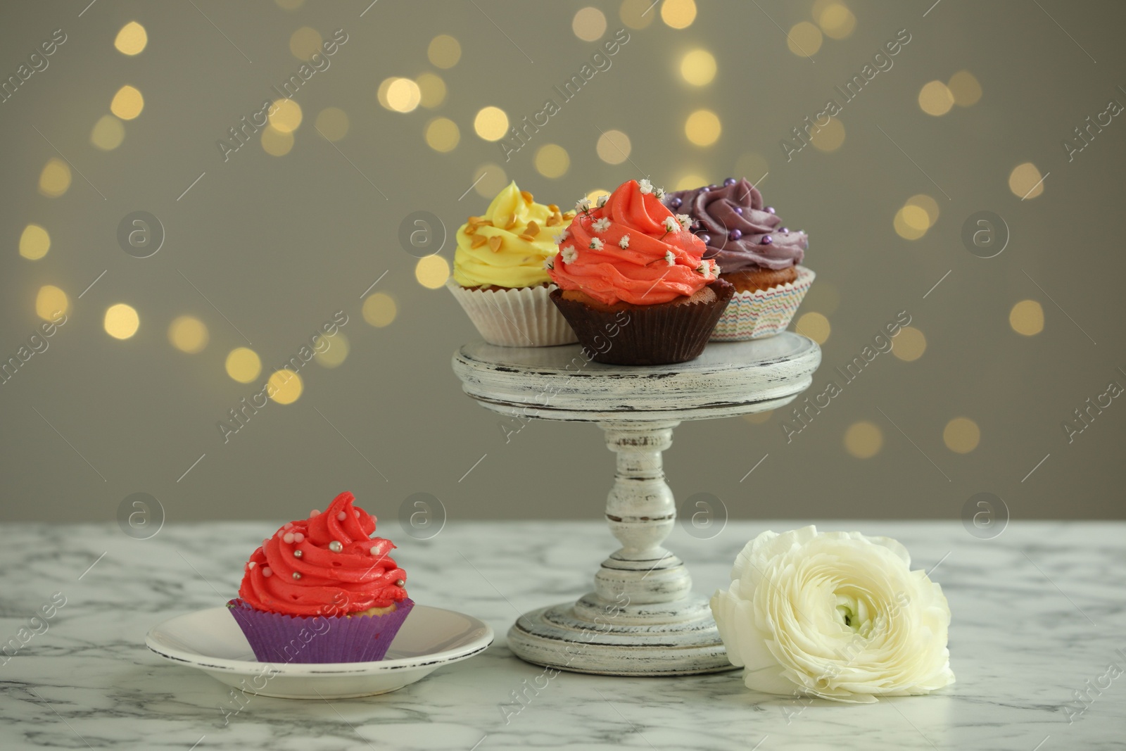 Photo of Different colorful cupcakes on white marble table against blurred lights