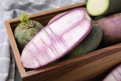 Photo of Purple and green daikon radishes in wooden crate on table, closeup