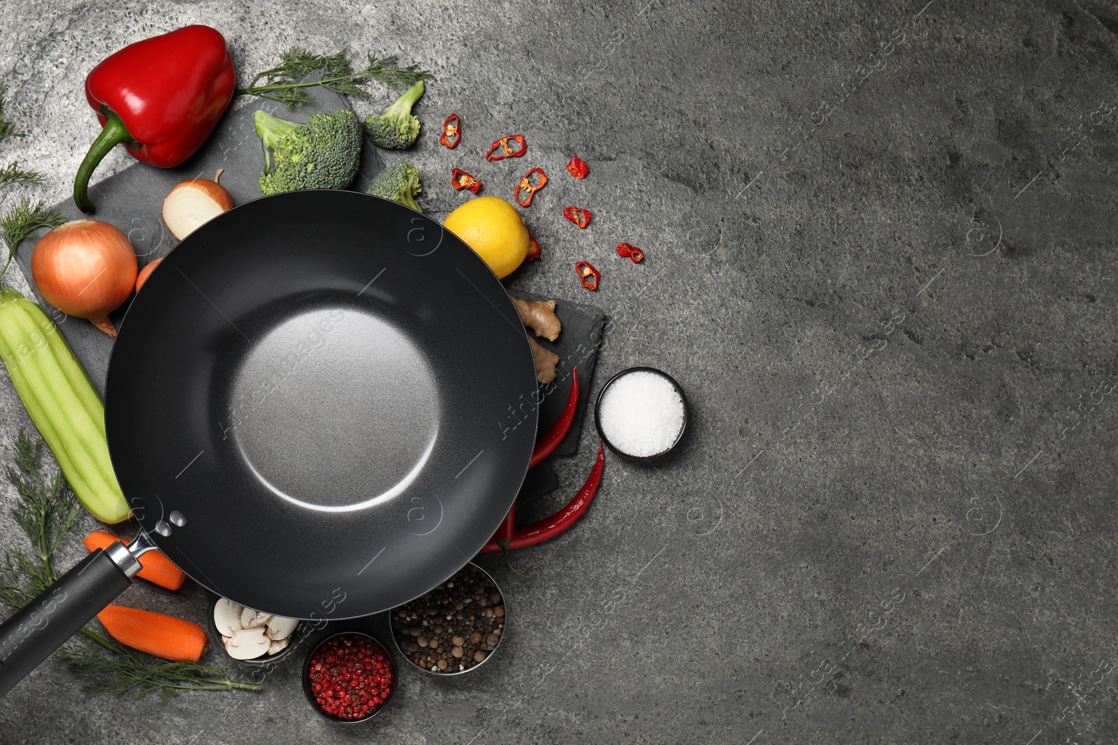 Photo of Empty iron wok surrounded by ingredients on grey table, flat lay. Space for text