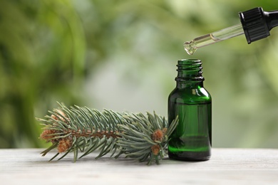 Photo of Bottle and pipette with conifer essential oil on table against blurred background. Space for text