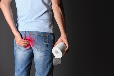 Image of Man with toilet paper suffering from hemorrhoid on black background, closeup. Space for text