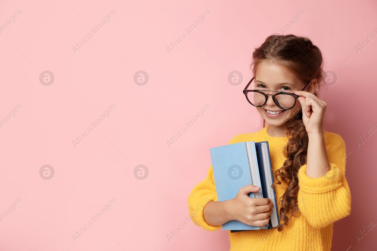 Photo of Cute little girl with glasses and books on pink background, space for text. Reading concept