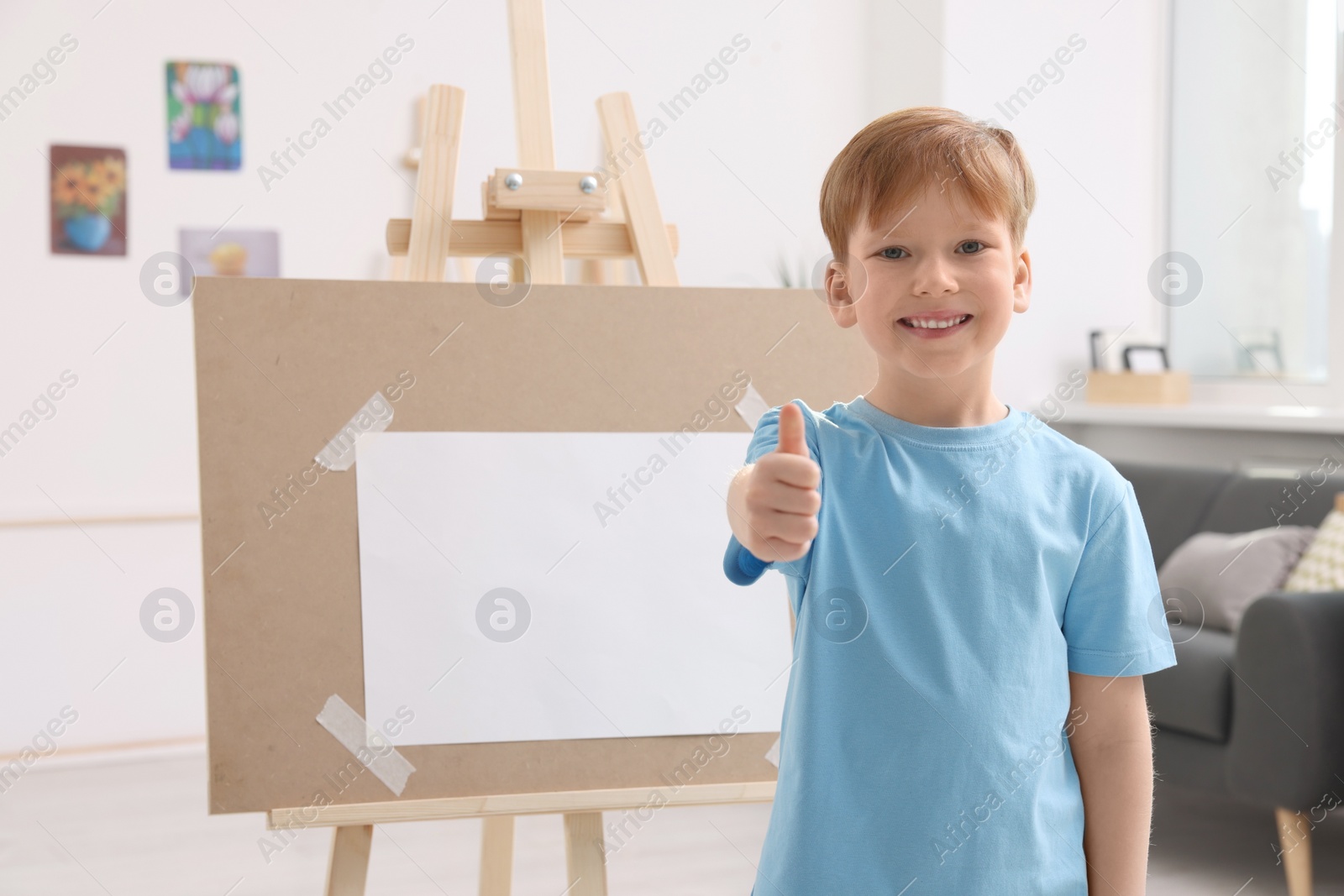 Photo of Happy little boy showing thumbs up in studio. Using easel to hold canvas