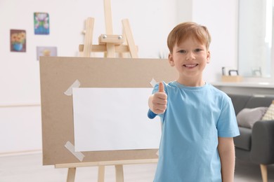 Happy little boy showing thumbs up in studio. Using easel to hold canvas