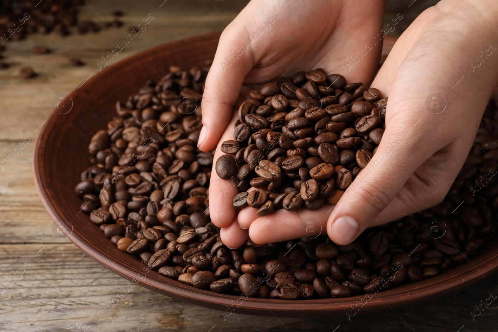 Photo of Woman taking pile of roasted coffee beans from bowl at wooden table, closeup