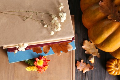 Stack of books with autumn leaves and flowers as bookmarks on wooden table, flat lay