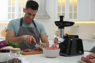 Photo of Man cutting meat in kitchen, focus on modern grinder