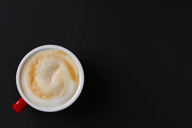 Photo of Cup with aromatic cappuccino on black background, top view. Space for text