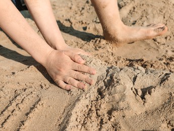 Photo of Little boy playing with sand on sunny day, closeup