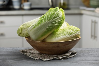 Photo of Fresh Chinese cabbages in bowl on grey wooden table indoors