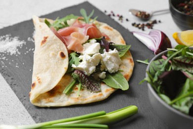 Photo of Delicious pita wrap with jamon, cheese cream and greens on light gray table, closeup