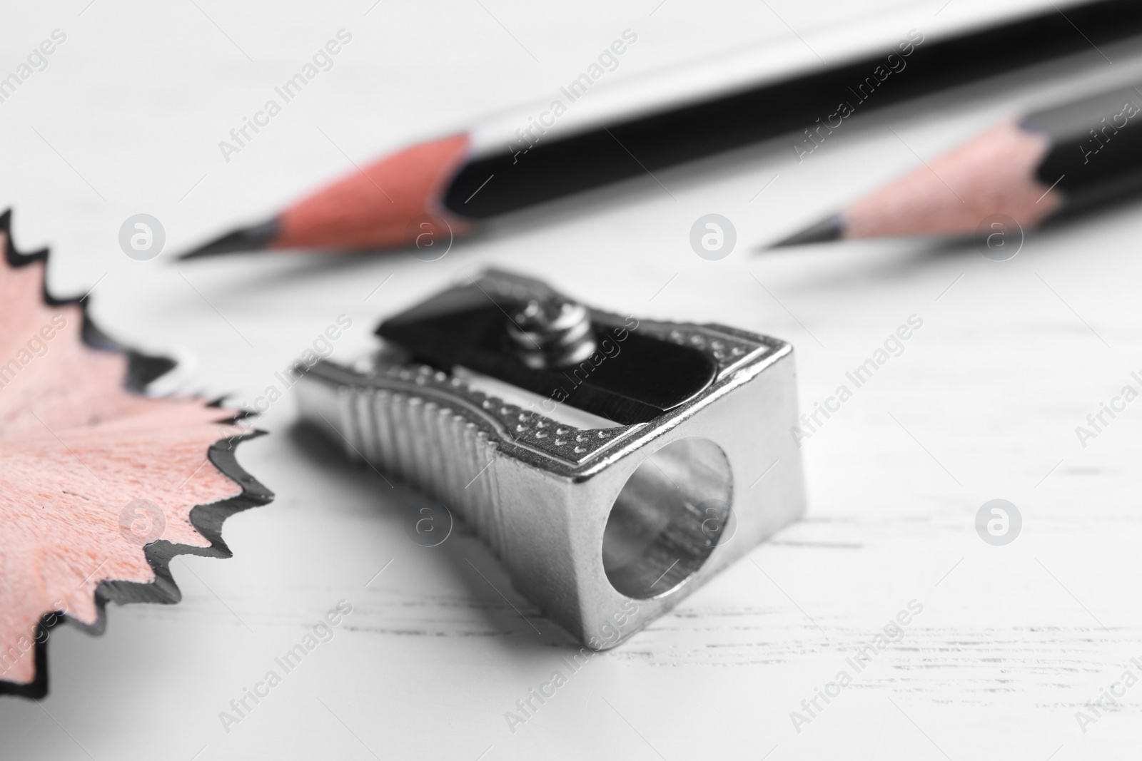 Photo of Pencils, sharpener and shavings on white wooden background, closeup