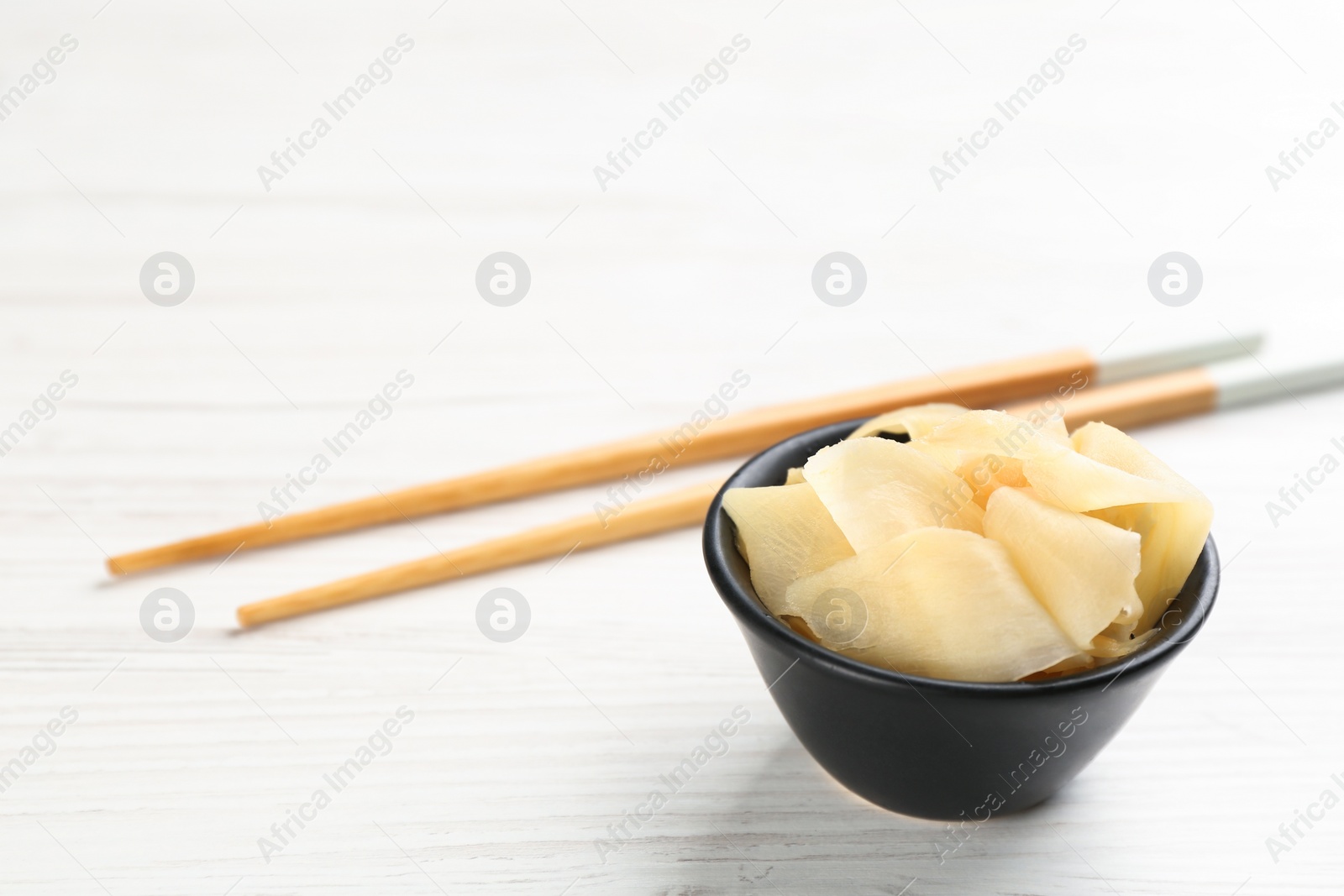 Photo of Spicy pickled ginger and chopsticks on white wooden table, space for text