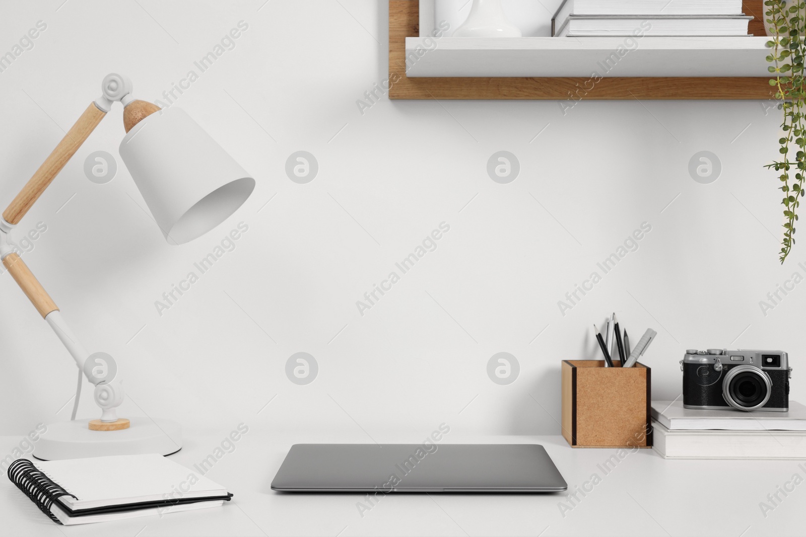 Photo of Home office. Laptop, vintage camera, lamp and stationery on white desk indoors