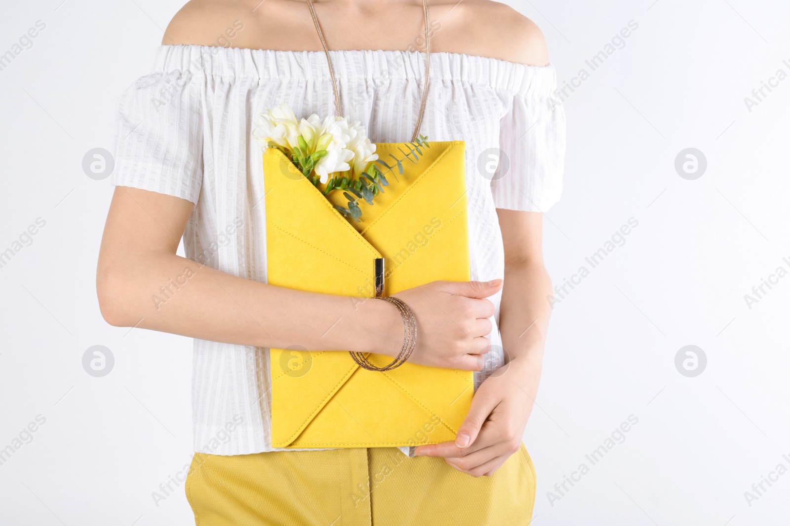 Photo of Stylish woman with clutch and spring flowers against light background, closeup