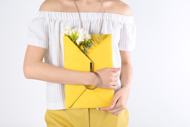 Photo of Stylish woman with clutch and spring flowers against light background, closeup