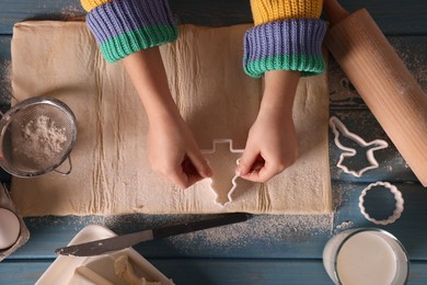 Photo of Little child cutting Christmas cookies at blue wooden table, top view