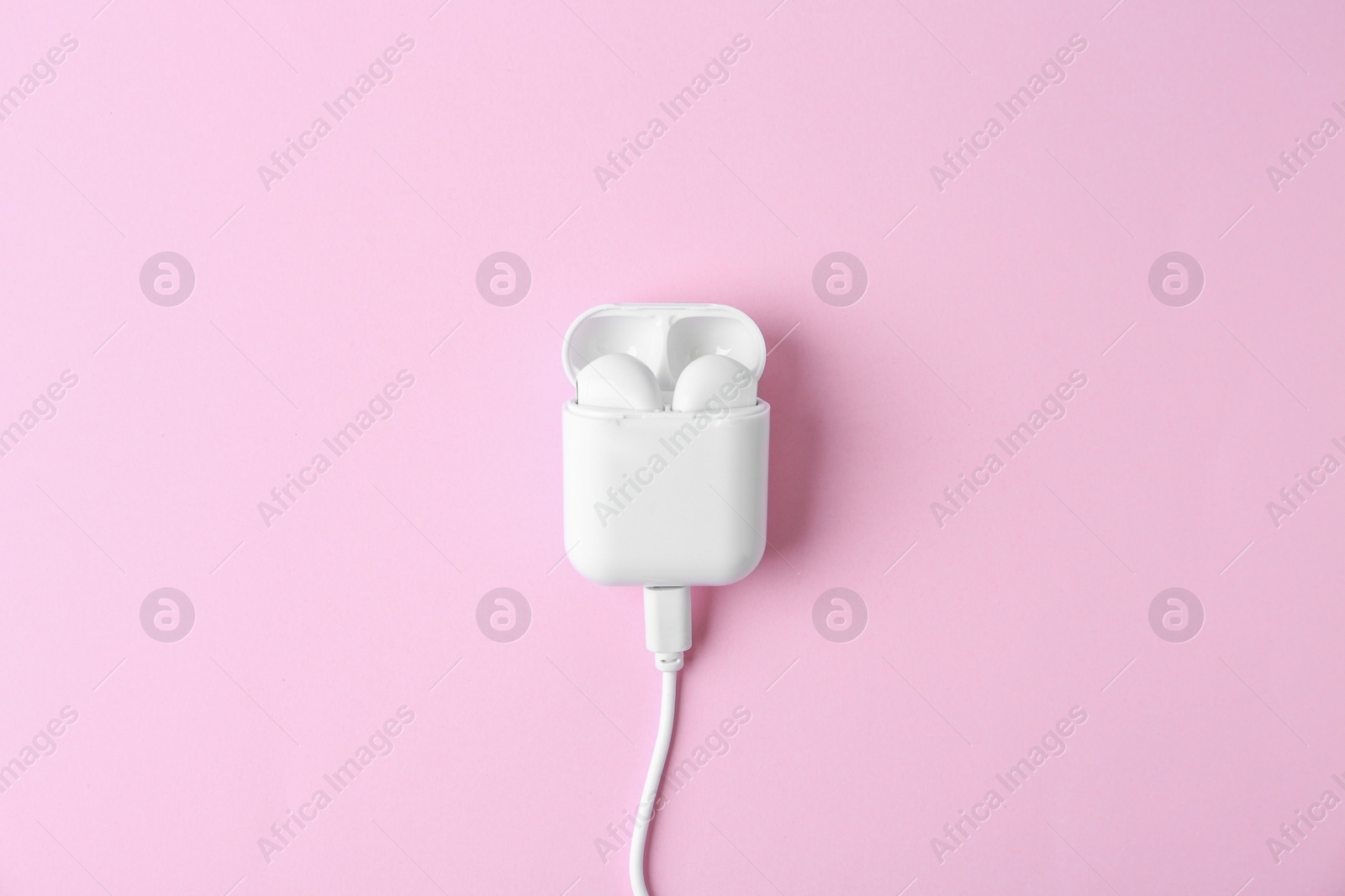 Photo of Modern wireless earphones in charging case with cable on pink background, top view