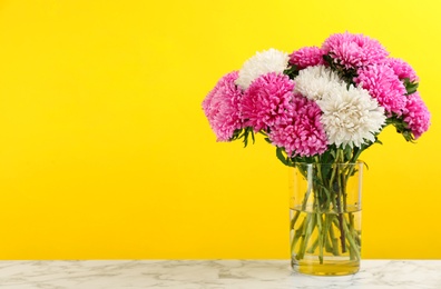 Photo of Beautiful asters in vase on table against yellow background, space for text. Autumn flowers