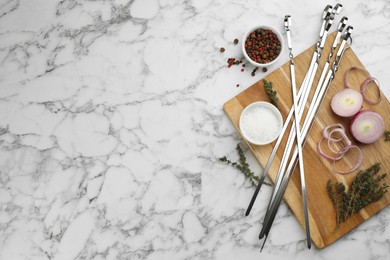 Flat lay composition with metal skewers on white marble table. Space for text