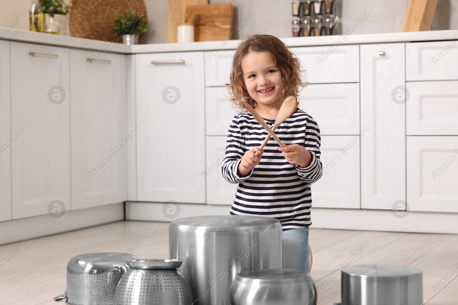 Photo of Little girl pretending to play drums on pots in kitchen