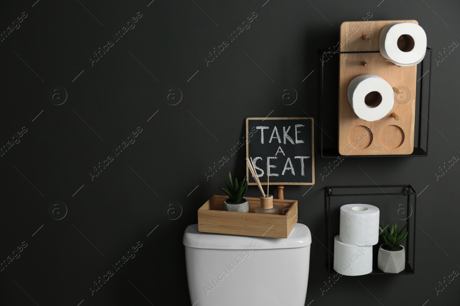 Photo of Decor elements, necessities and toilet bowl near black wall, space for text. Bathroom interior