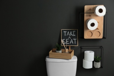 Photo of Decor elements, necessities and toilet bowl near black wall, space for text. Bathroom interior