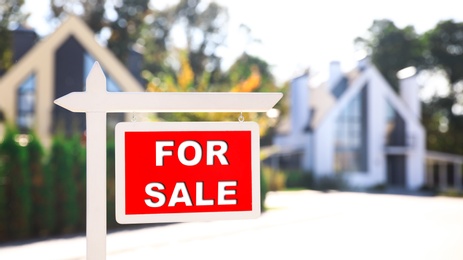 Red real estate sign near house outdoors on sunny day