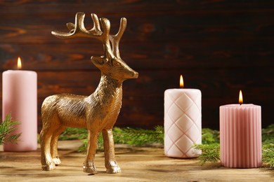 Photo of Beautiful deer figure and burning candles on wooden table, closeup