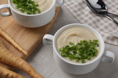 Photo of Bowls with tasty creamy soup of parsnip served on light grey table, closeup