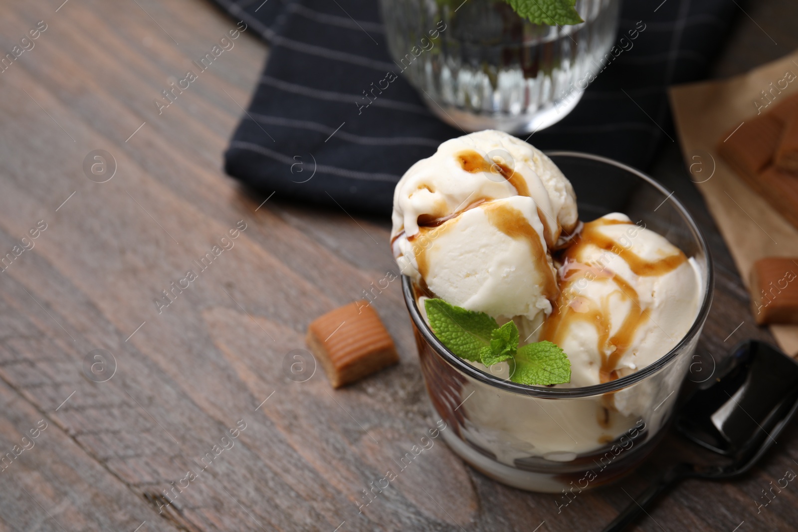 Photo of Scoops of ice cream with caramel sauce, mint leaves and candies on wooden table, closeup. Space for text
