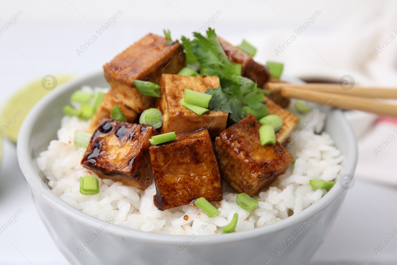 Photo of Bowl of rice with fried tofu and greens on white table, closeup
