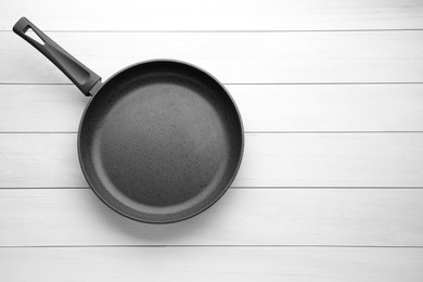Photo of New non-stick frying pan on white wooden table, top view. Space for text