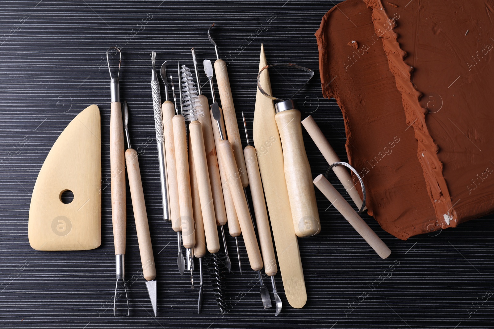 Photo of Clay and set of modeling tools on dark gray wooden table, flat lay