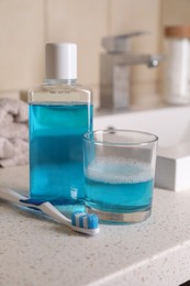 Photo of Bottle with fresh mouthwash, glass and dental floss on countertop in bathroom