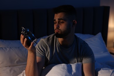 Sleepy man looking at alarm clock in bed