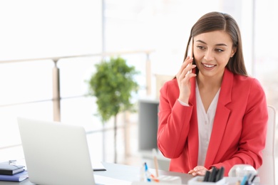 Photo of Young woman talking on phone at workplace