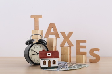 Photo of Word TAXES, money, house model and alarm clock on table