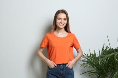 Young woman wearing blank t-shirt on light background. Mockup for design