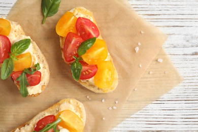 Delicious tomato bruschettas on white wooden background, top view. Space for text