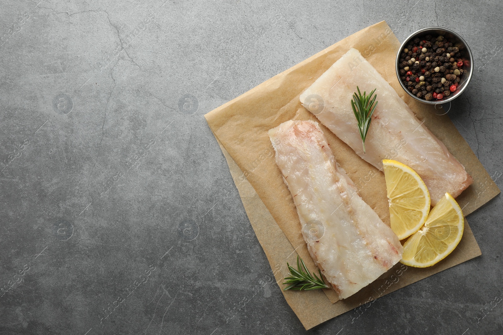 Photo of Fresh raw cod fillets, spices and lemon slices on grey table, flat lay. Space for text