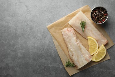 Fresh raw cod fillets, spices and lemon slices on grey table, flat lay. Space for text
