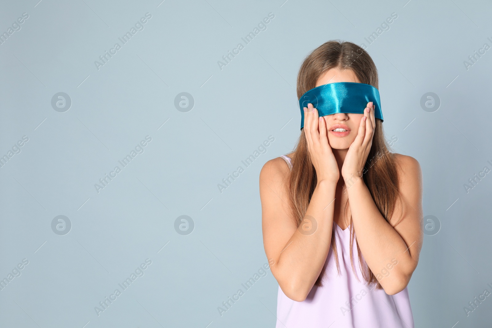 Photo of Young woman with light blue blindfold on grey background