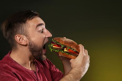 Photo of Young man eating tasty burger on color background. Space for text