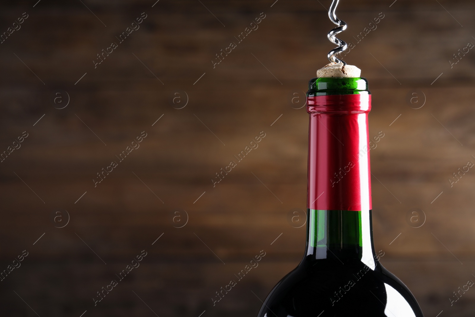 Photo of Opening wine bottle with corkscrew on dark brown background, closeup. Space for text