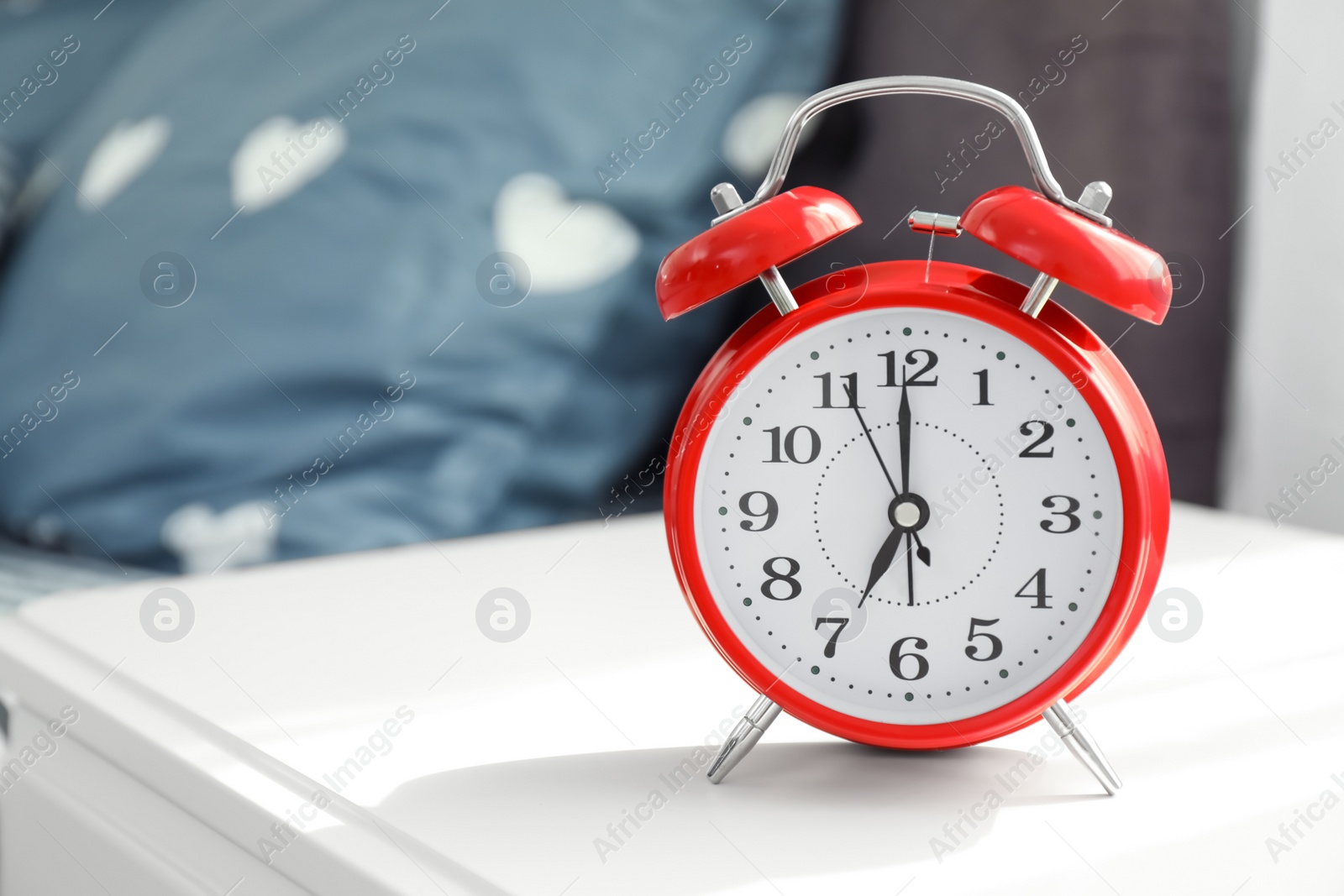 Photo of Analog alarm clock on table in bedroom. Time of day