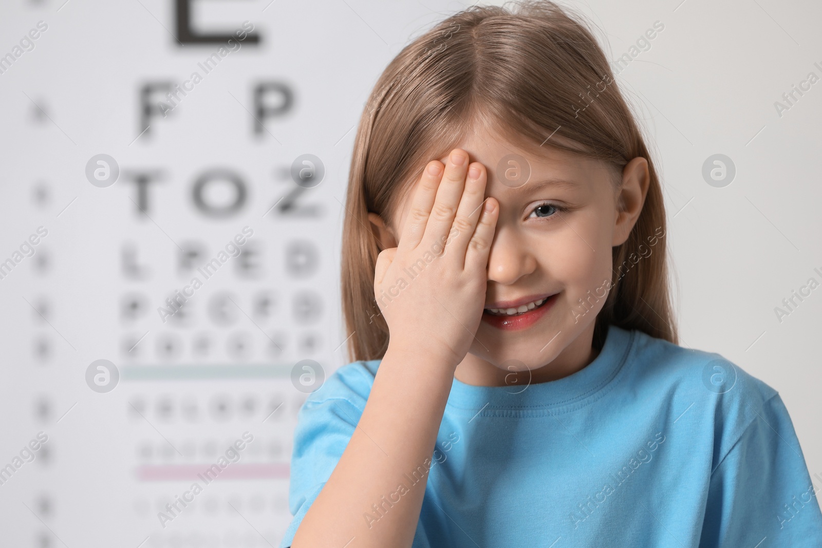 Photo of Little girl covering her eye against vision test chart